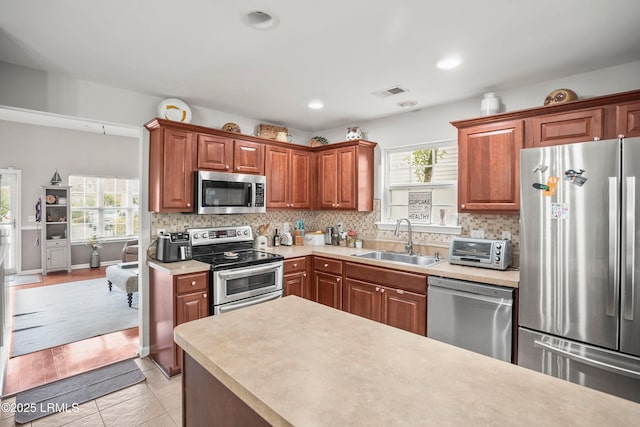 kitchen featuring stainless steel appliances, light countertops, a sink, and tasteful backsplash