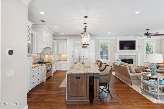 kitchen with pendant lighting, an island with sink, white cabinetry, a kitchen breakfast bar, and light stone counters