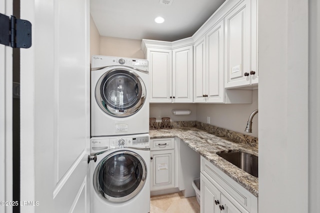 laundry area featuring cabinets, stacked washer / drying machine, and sink