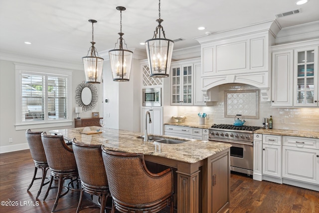 kitchen featuring sink, appliances with stainless steel finishes, ornamental molding, an island with sink, and white cabinets