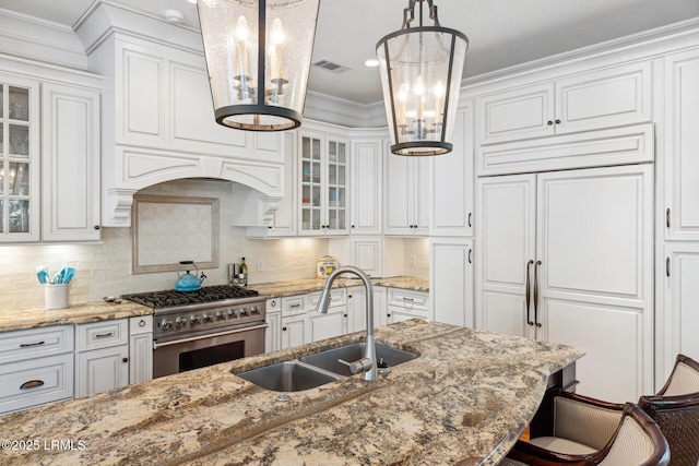 kitchen featuring sink, high end appliances, decorative light fixtures, light stone countertops, and white cabinets