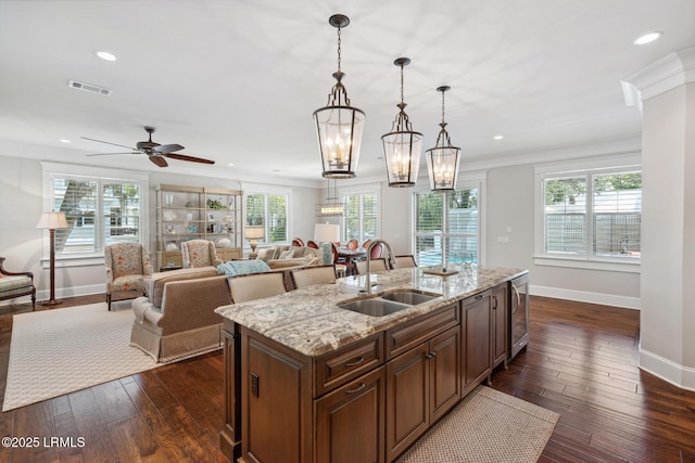 kitchen with decorative light fixtures, sink, a kitchen island with sink, light stone counters, and crown molding