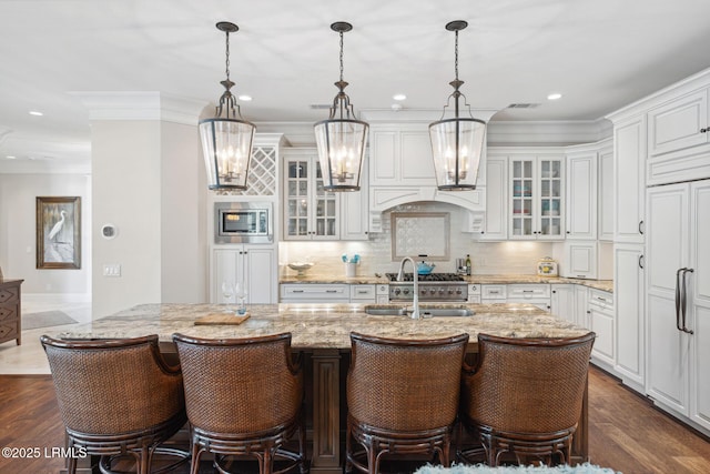 kitchen with white cabinetry, light stone countertops, sink, and a center island with sink