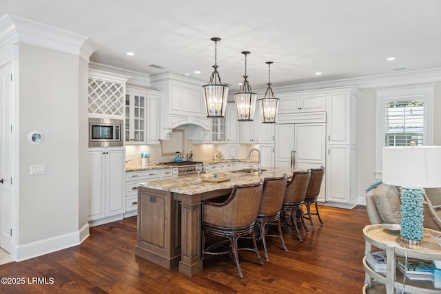 kitchen featuring pendant lighting, sink, a kitchen island with sink, light stone counters, and white cabinets