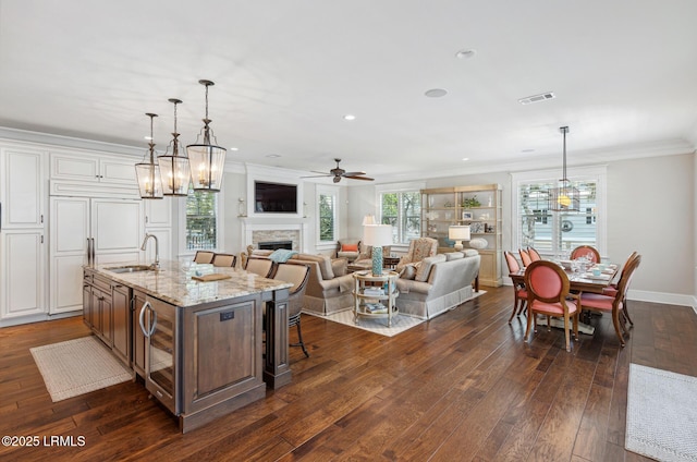 kitchen with white cabinetry, sink, a kitchen bar, a kitchen island with sink, and light stone countertops