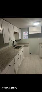 kitchen with light stone counters, a sink, and white cabinetry