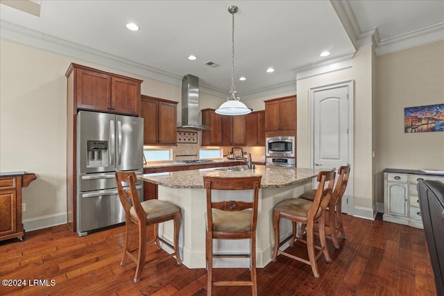 kitchen featuring pendant lighting, wall chimney range hood, stainless steel appliances, light stone countertops, and a center island with sink