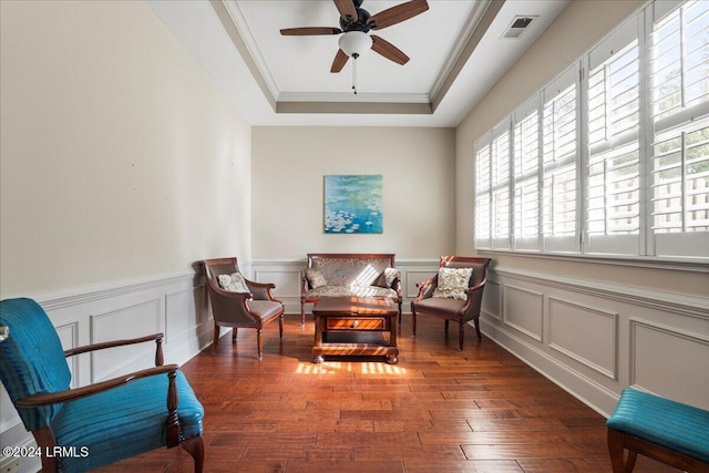 living area with a raised ceiling, crown molding, dark wood-type flooring, and ceiling fan