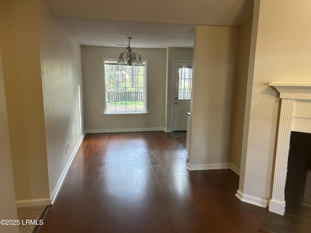 unfurnished dining area with a fireplace, an inviting chandelier, dark wood-type flooring, a textured ceiling, and baseboards