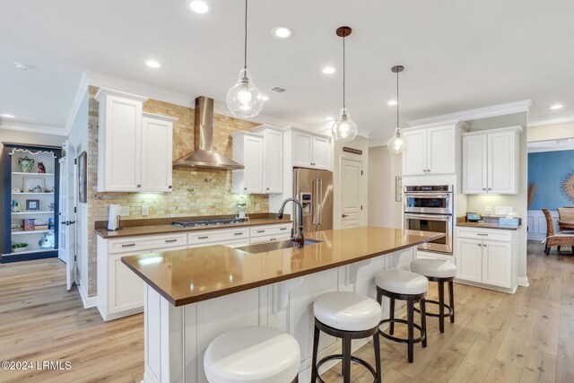 kitchen featuring pendant lighting, sink, white cabinets, stainless steel appliances, and wall chimney exhaust hood