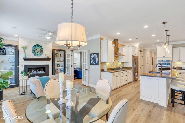 dining room featuring crown molding, a fireplace, light wood-type flooring, and french doors