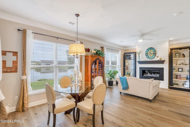 dining area featuring ornamental molding, a large fireplace, ceiling fan, and light hardwood / wood-style floors