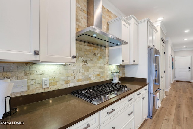 kitchen featuring white cabinetry, appliances with stainless steel finishes, wall chimney range hood, and decorative backsplash