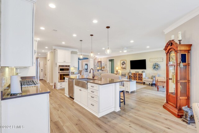 kitchen with sink, a center island with sink, pendant lighting, stainless steel appliances, and white cabinets