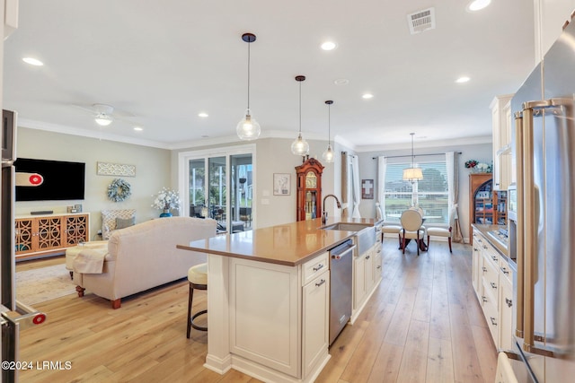 kitchen with a breakfast bar area, appliances with stainless steel finishes, an island with sink, pendant lighting, and white cabinets