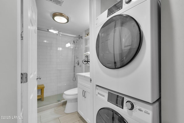 bathroom featuring stacked washer and dryer, a shower with door, tile walls, vanity, and toilet