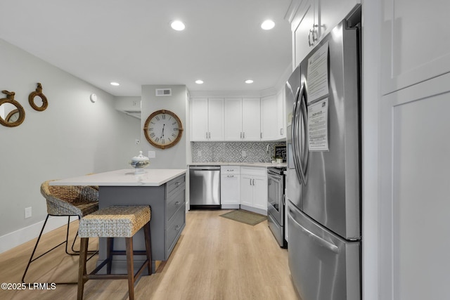 kitchen featuring appliances with stainless steel finishes, a breakfast bar, white cabinets, a center island, and light hardwood / wood-style flooring