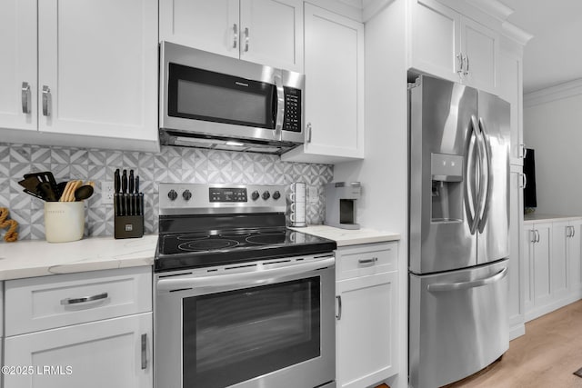 kitchen with appliances with stainless steel finishes, white cabinetry, tasteful backsplash, light stone countertops, and light wood-type flooring