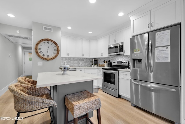 kitchen with tasteful backsplash, appliances with stainless steel finishes, white cabinets, and a kitchen breakfast bar