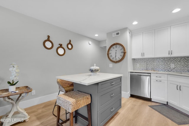 kitchen featuring a center island, stainless steel dishwasher, a kitchen breakfast bar, light stone countertops, and white cabinets