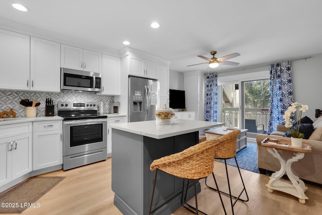 kitchen featuring white cabinetry, a kitchen bar, a center island, stainless steel appliances, and light hardwood / wood-style flooring