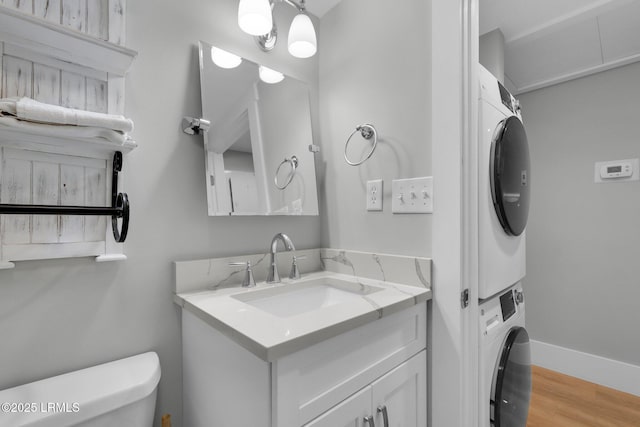 bathroom with stacked washer / dryer, vanity, hardwood / wood-style flooring, and toilet