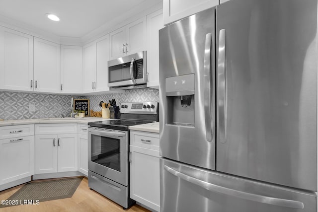 kitchen featuring backsplash, appliances with stainless steel finishes, light wood-type flooring, and white cabinets