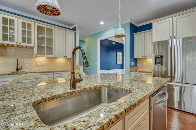 kitchen with sink, crown molding, light stone counters, appliances with stainless steel finishes, and pendant lighting