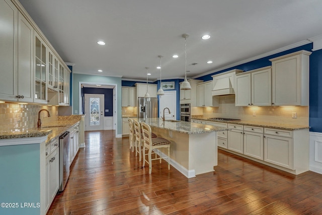 kitchen featuring dark wood-type flooring, a breakfast bar area, appliances with stainless steel finishes, pendant lighting, and a kitchen island with sink