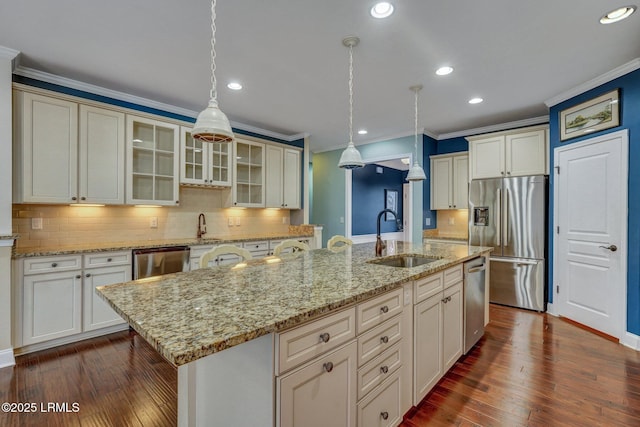 kitchen with appliances with stainless steel finishes, decorative light fixtures, sink, dark wood-type flooring, and a spacious island