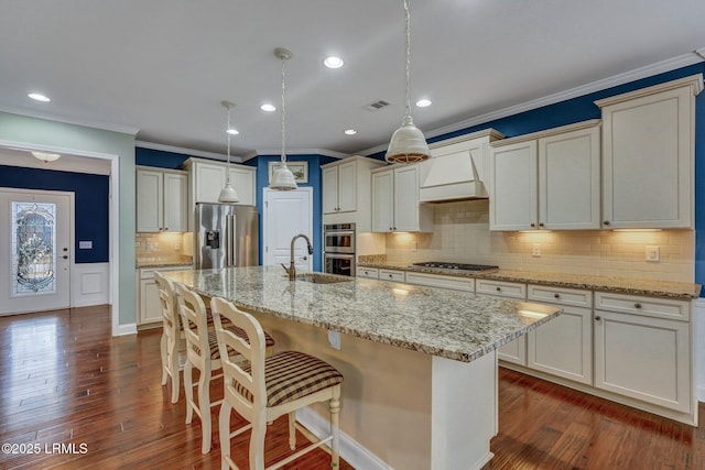 kitchen featuring premium range hood, sink, hanging light fixtures, a center island with sink, and stainless steel appliances