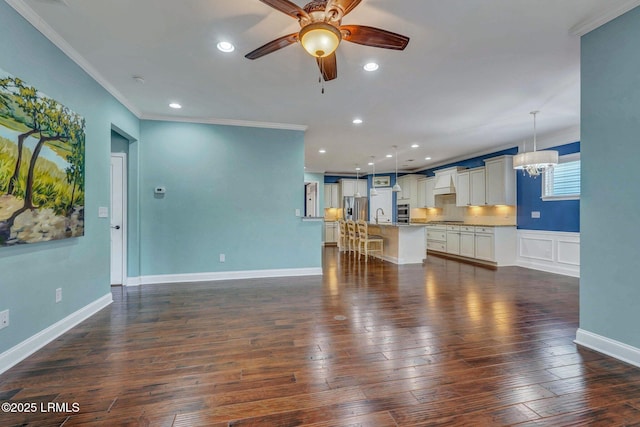 unfurnished living room featuring ceiling fan with notable chandelier, ornamental molding, dark hardwood / wood-style floors, and sink