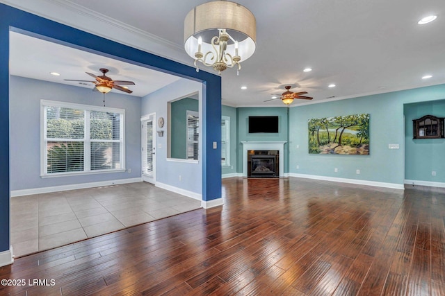 unfurnished living room featuring ceiling fan with notable chandelier, wood-type flooring, and ornamental molding