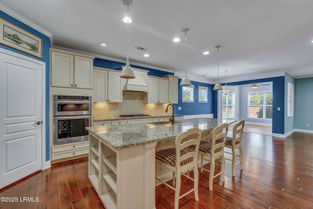 kitchen with a breakfast bar area, hanging light fixtures, stainless steel appliances, light stone countertops, and a center island with sink