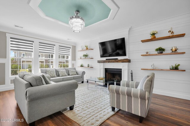 living room featuring crown molding, a fireplace with flush hearth, wood finished floors, and a healthy amount of sunlight