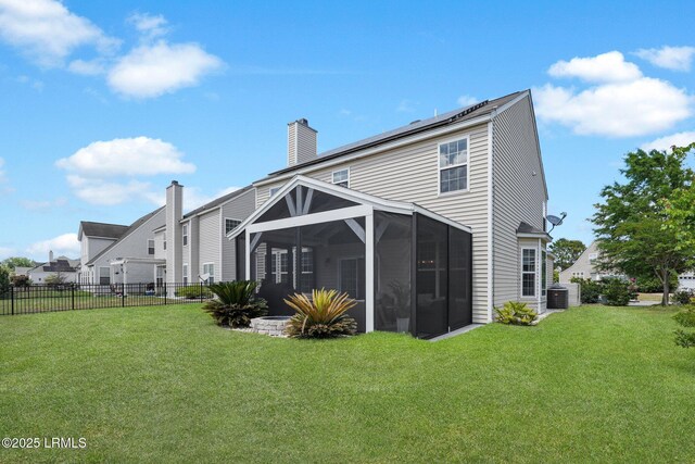 back of house with a chimney, a lawn, a sunroom, central AC, and fence