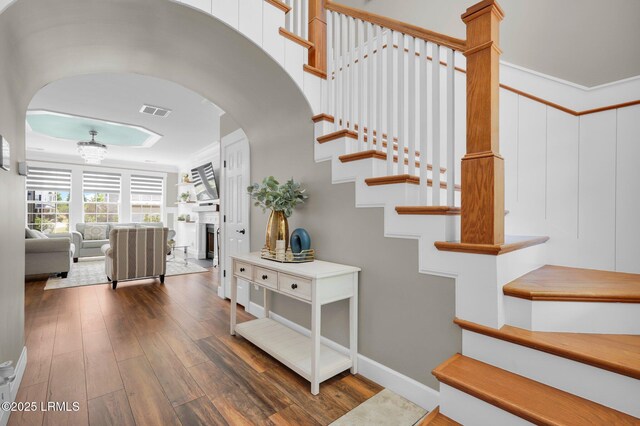 stairs featuring visible vents, ornamental molding, a fireplace, hardwood / wood-style floors, and arched walkways