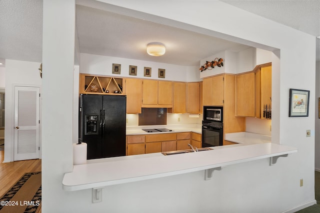 kitchen featuring sink, a textured ceiling, a kitchen breakfast bar, kitchen peninsula, and black appliances