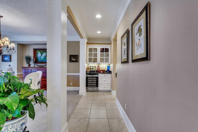 corridor with light tile patterned flooring, wine cooler, a chandelier, ornamental molding, and a textured ceiling