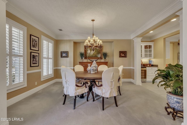 carpeted dining area featuring wine cooler, ornate columns, a textured ceiling, ornamental molding, and a notable chandelier