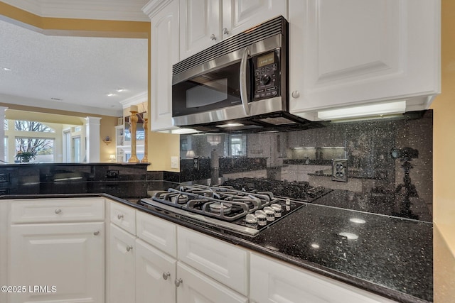 kitchen featuring crown molding, white cabinetry, dark stone countertops, stainless steel appliances, and decorative backsplash