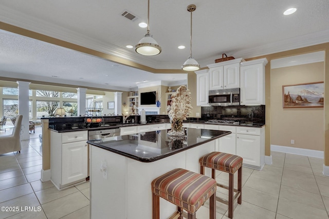 kitchen with white cabinetry, stainless steel appliances, a kitchen bar, kitchen peninsula, and ornate columns