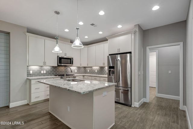 kitchen featuring appliances with stainless steel finishes, white cabinetry, hanging light fixtures, a kitchen island with sink, and light wood-type flooring