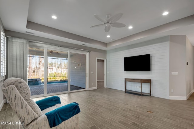 living room with a raised ceiling and ceiling fan