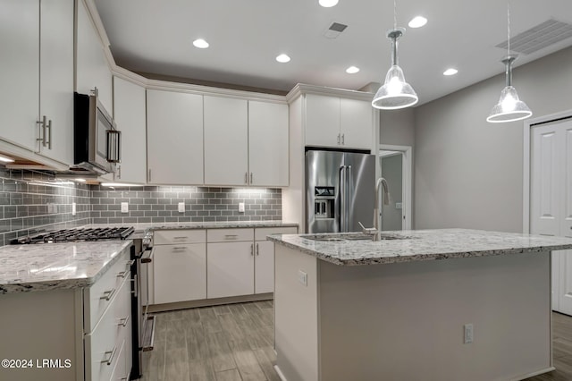 kitchen featuring decorative light fixtures, an island with sink, white cabinets, stainless steel appliances, and light wood-type flooring