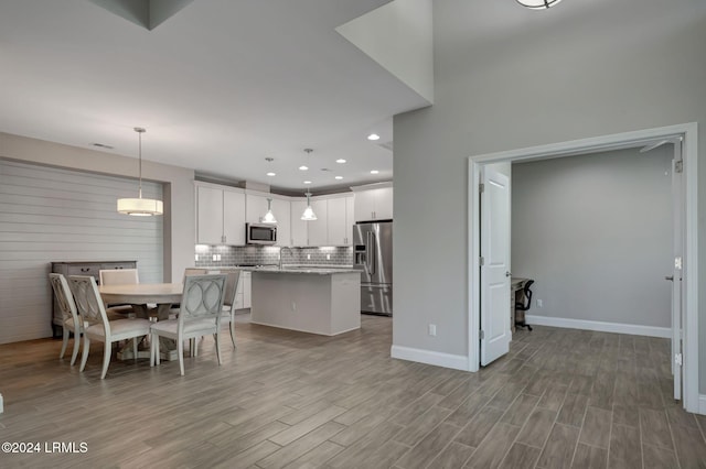 kitchen featuring a kitchen island, decorative light fixtures, white cabinetry, stainless steel appliances, and light wood-type flooring