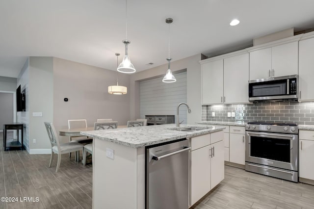 kitchen featuring sink, appliances with stainless steel finishes, a kitchen island with sink, white cabinets, and decorative light fixtures