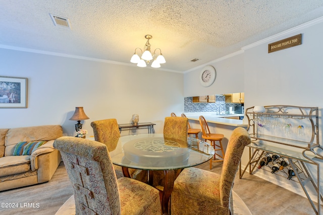 dining space featuring ornamental molding, light wood-type flooring, a chandelier, and a textured ceiling