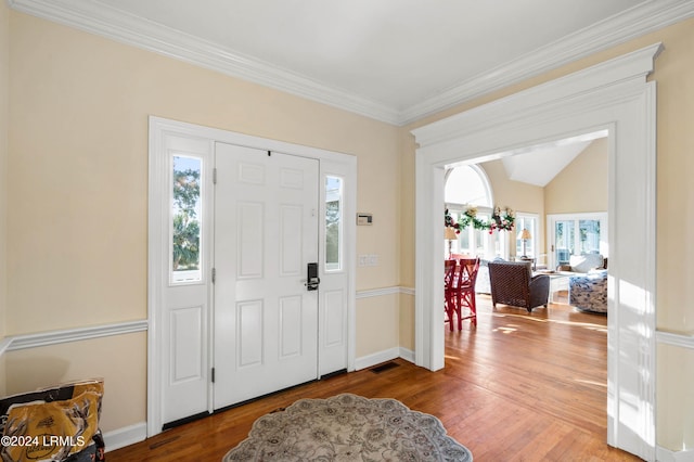 foyer entrance featuring vaulted ceiling, ornamental molding, a healthy amount of sunlight, and hardwood / wood-style floors