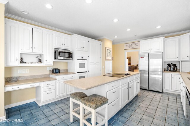 kitchen featuring built in desk, white cabinetry, ornamental molding, a center island, and stainless steel appliances